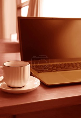 Photo for Red Brown Colored Cup of Coffee with Blurry Opened Laptop in the Backdrop - Royalty Free Image
