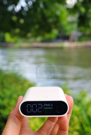 Téléchargez les photos : Main tenant un capteur de pollution atmosphérique mesurant la qualité de l'air dans le jardin riverain - en image libre de droit