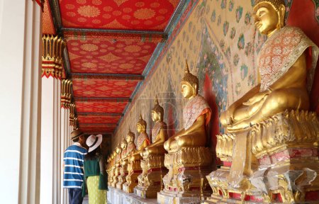 Foto de Parejas en el claustro con un gran grupo de magníficas imágenes de Buda dorada sentada en Wat Arun o el templo de Dawn, Bangkok, Tailandia - Imagen libre de derechos