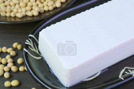 Téléchargez les photos : Gros plan d'un caillé de haricot de tofu mou avec une pile de soja séchée floue en arrière-plan - en image libre de droit