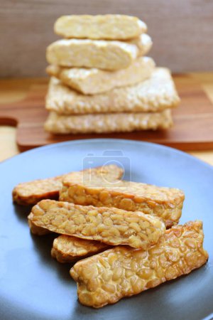 Plate of pan fried Tempeh with Stack of the Uncooked in the Backdrop