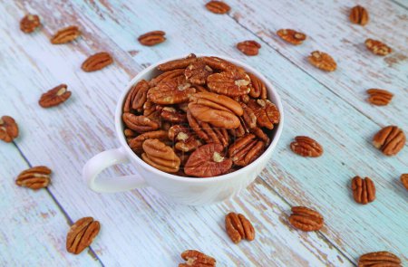 Cup Full of Pecan Nuts with Some Kernels Scattered on Wooden Table