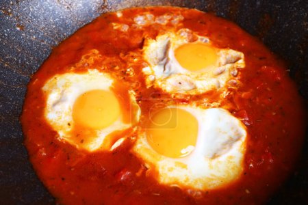Shakshuka, huevos escalfados en salsa de tomate sabrosa durante la cocción en una sartén de hierro fundido
