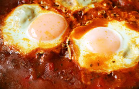 Großaufnahme von Eiern, die in gewürzter Tomatensauce für Shakshuka pochiert werden