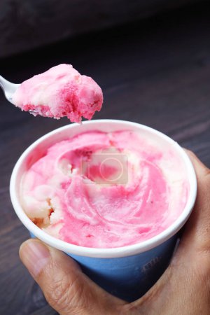 Spoon scooping delectable strawberry yogurt ice cream from a cup