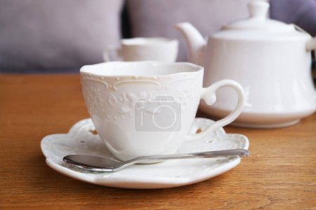 Taza blanca con té empapado en una tetera en el telón de fondo