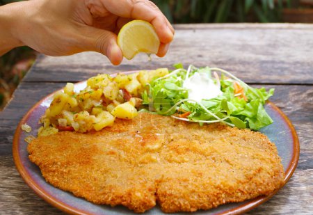 Hand Squeezing a Slice of Lemon on the Freshly Fried Schnitzel