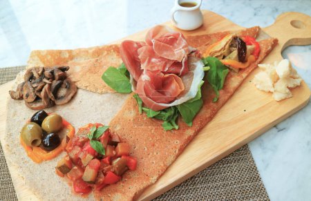 Appetizer Crepe or Crepe Antipasto with cold cuts and variety of saute vegetables served on wooden breadboard