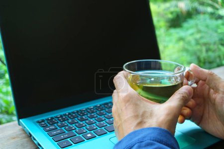Mann hält eine Tasse Tee, während er an seinem Laptop arbeitet