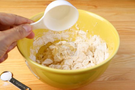 Hand pouring olive oil into the kneaded mixture of bread dough