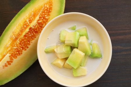 Thai-Melone in gekühlter gesüßter Kokosmilch mit einer Scheibe frischem Obst auf schwarzem Holzhintergrund