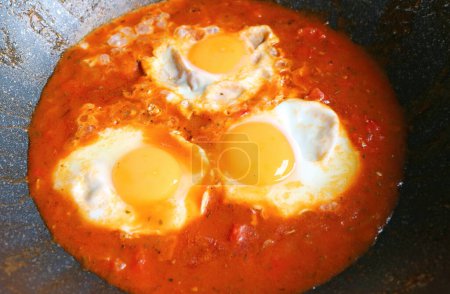 Closeup of eggs being poached in spiced tomato sauce for Shakshuka Dish