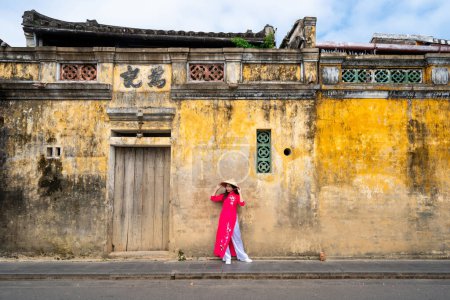 Foto de Young female tourist in Vietnamese traditional dress walking at Hoi An Ancient town in Vietnam - Imagen libre de derechos