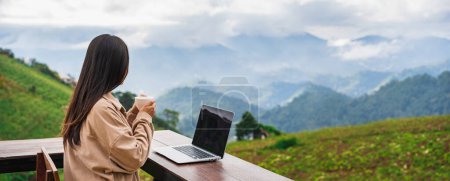 Junge Freiberuflerin arbeitet online mit Laptop und genießt die schöne Naturlandschaft mit Bergblick