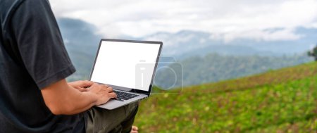 Junger Mann freiberuflicher Reisender arbeitet online mit Laptop und genießt die schöne Naturlandschaft mit Bergblick