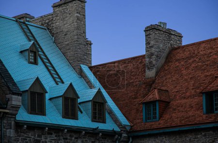 Techos coloridos con ventanas de dormitorios y chimeneas de piedra de edificios residenciales contra un cielo azul en el histórico Old Quebec en Quebec City, Canadá