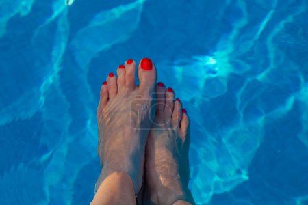Female feet with red polished toe nails immersed in a blue water pool