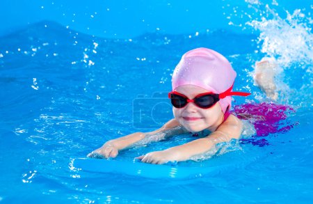 Foto de Niña aprendiendo a nadar en piscina cubierta con tabla flotante de la piscina - Imagen libre de derechos