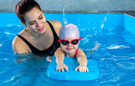 Foto de Niña aprendiendo a nadar en piscina cubierta con tabla de billar. Niño activo nada en el agua con el maestro - Imagen libre de derechos
