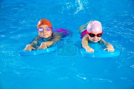 Foto de Two little girls having fun in pool learning how to swim using flutterboards - Imagen libre de derechos
