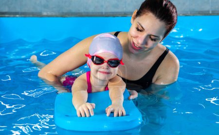 Foto de Niña aprendiendo a nadar en piscina cubierta con tabla de billar. Niño activo nada en el agua con el maestro - Imagen libre de derechos