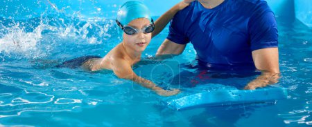 Foto de Male trainer teaching boy how to swim in indoor pool with pool flutter board - Imagen libre de derechos