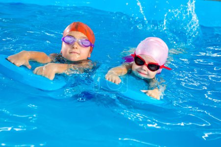 Two little girls having fun in pool learning how to swim using flutterboards