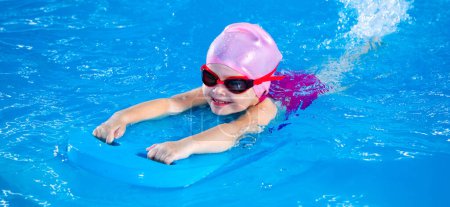 Foto de Smiling little girl learning to swim in indoor pool with flutter board during swimming class - Imagen libre de derechos