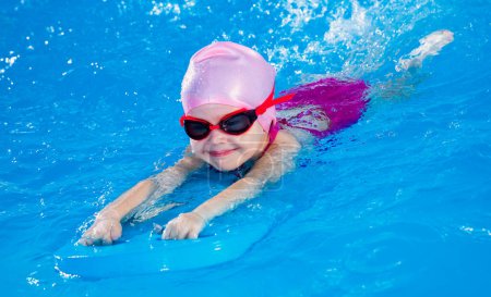Foto de Preescolar linda chica aprendiendo a nadar en la piscina cubierta con flautista - Imagen libre de derechos