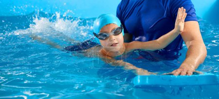 Foto de Niño aprendiendo a nadar en piscina cubierta con tabla de billar. Clase de natación. Niño activo nada en el agua con el maestro - Imagen libre de derechos