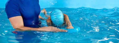 Foto de Entrenador masculino enseñando a nadar en la piscina cubierta con tabla de aleteo de la piscina - Imagen libre de derechos