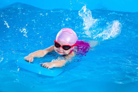 Foto de Preschool cute girl learning to swim in indoor pool with flutterboard - Imagen libre de derechos