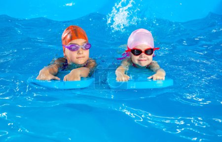 Foto de Two little girls having fun in pool learning how to swim using flutterboards - Imagen libre de derechos