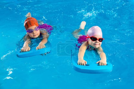 Foto de Dos niñas divirtiéndose en la piscina aprendiendo a nadar usando flautas - Imagen libre de derechos
