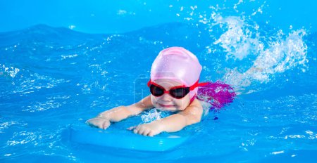 Foto de Niña aprendiendo a nadar en piscina cubierta con tabla flotante de la piscina - Imagen libre de derechos