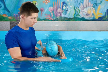 Foto de Little boy learning to swim in indoor pool with pool board. Swimming lesson. Active child swims in water with teacher - Imagen libre de derechos