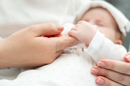 Foto de Close-up muestra un bebé recién nacido enfermo tiernamente agarrando el dedo de las madres, toalla húmeda descansando sobre su frente - Imagen libre de derechos