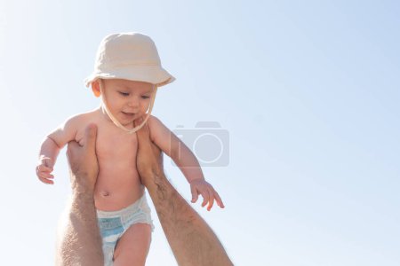 Foto de El amor de un padre es evidente mientras sostiene a su bebé en alto, su risa resonando bajo el cielo iluminado por el sol. Concepto de inocencia y paternidad alegre - Imagen libre de derechos