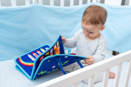 Bebé de un año jugando con montessori libro ocupado sentado en la cuna