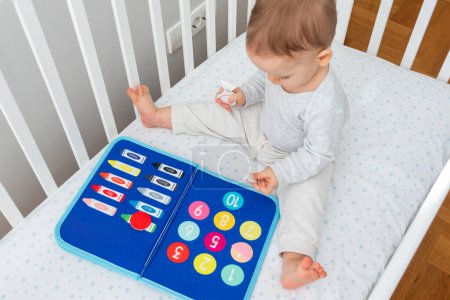 Alegría de aprender en la primera infancia con un bebé que interactúa con un libro ocupado Montessori en una cuna, combinando perfectamente los conceptos de libros inteligentes y juguetes educativos modernos para el desarrollo temprano