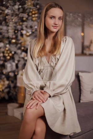 Photo for Christmas photo of beautiful girl with blond hair in elegant dress posing in cosy decorated studio with Christmas tree and presents - Royalty Free Image