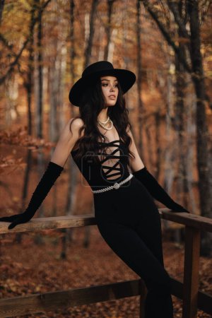 Foto de Foto de moda al aire libre de la hermosa mujer con el pelo oscuro en ropa elegante y accesorios posando en el bosque de otoño - Imagen libre de derechos
