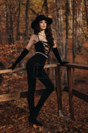 Foto de Foto de moda al aire libre de la hermosa mujer con el pelo oscuro en ropa elegante y accesorios posando en el bosque de otoño - Imagen libre de derechos