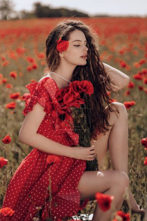 Foto de Foto de moda al aire libre de la hermosa mujer con el pelo oscuro en vestido rojo elegante posando en el campo de amapola en flor - Imagen libre de derechos