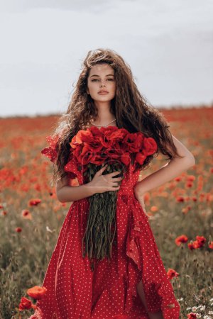 Téléchargez les photos : Photo de mode en plein air de belle femme aux cheveux foncés dans une élégante robe rouge posant dans un champ de pavot en fleurs - en image libre de droit