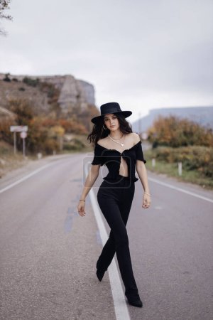 Photo for Fashion outdoor photo of beautiful woman with dark hair in elegant outfit posing on the road in mountains - Royalty Free Image