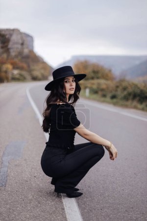 Téléchargez les photos : Fashion outdoor photo of beautiful woman with dark hair in elegant outfit posing on the road in mountains - en image libre de droit