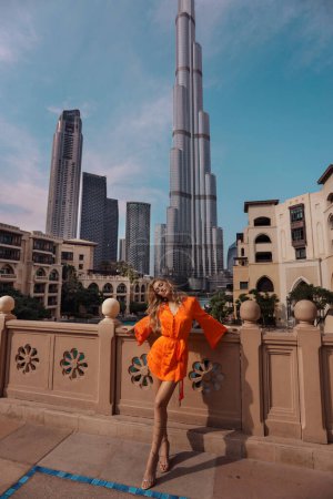 Foto de Fashion outdoor photo of beautiful woman with blond hair in elegant dress posing on the embankment with skyscrapers on the background - Imagen libre de derechos