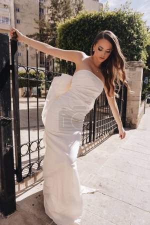 Photo for Fashion outdoor photo of beautiful woman with dark hair in luxurious wedding dress with accessories posing in the street of antic city - Royalty Free Image