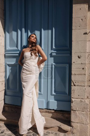 Photo for Fashion outdoor photo of beautiful woman with dark hair in luxurious wedding dress with accessories posing in the street of antic city - Royalty Free Image